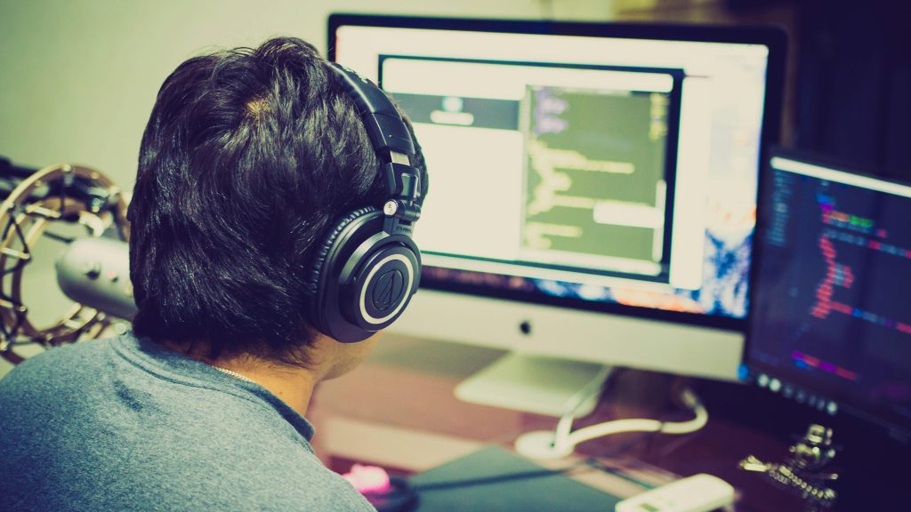 pexels-photo-340152-340152 A programmer with headphones focuses on coding at a computer setup with dual monitors.